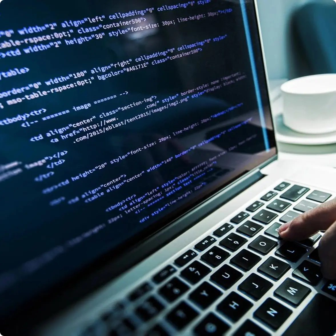 A person typing on a laptop displaying HTML code.