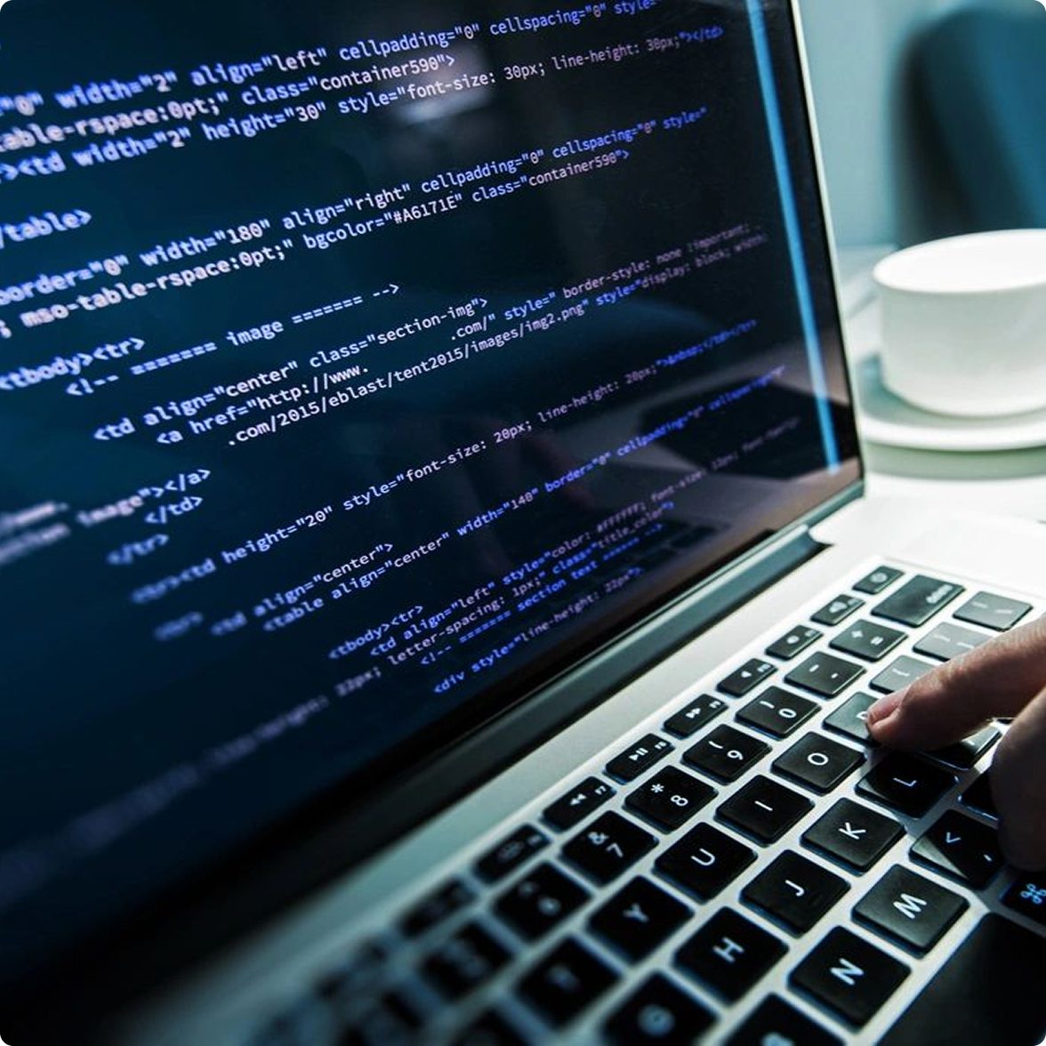 Rectangle 3 (1) A person typing on a laptop displaying HTML code.